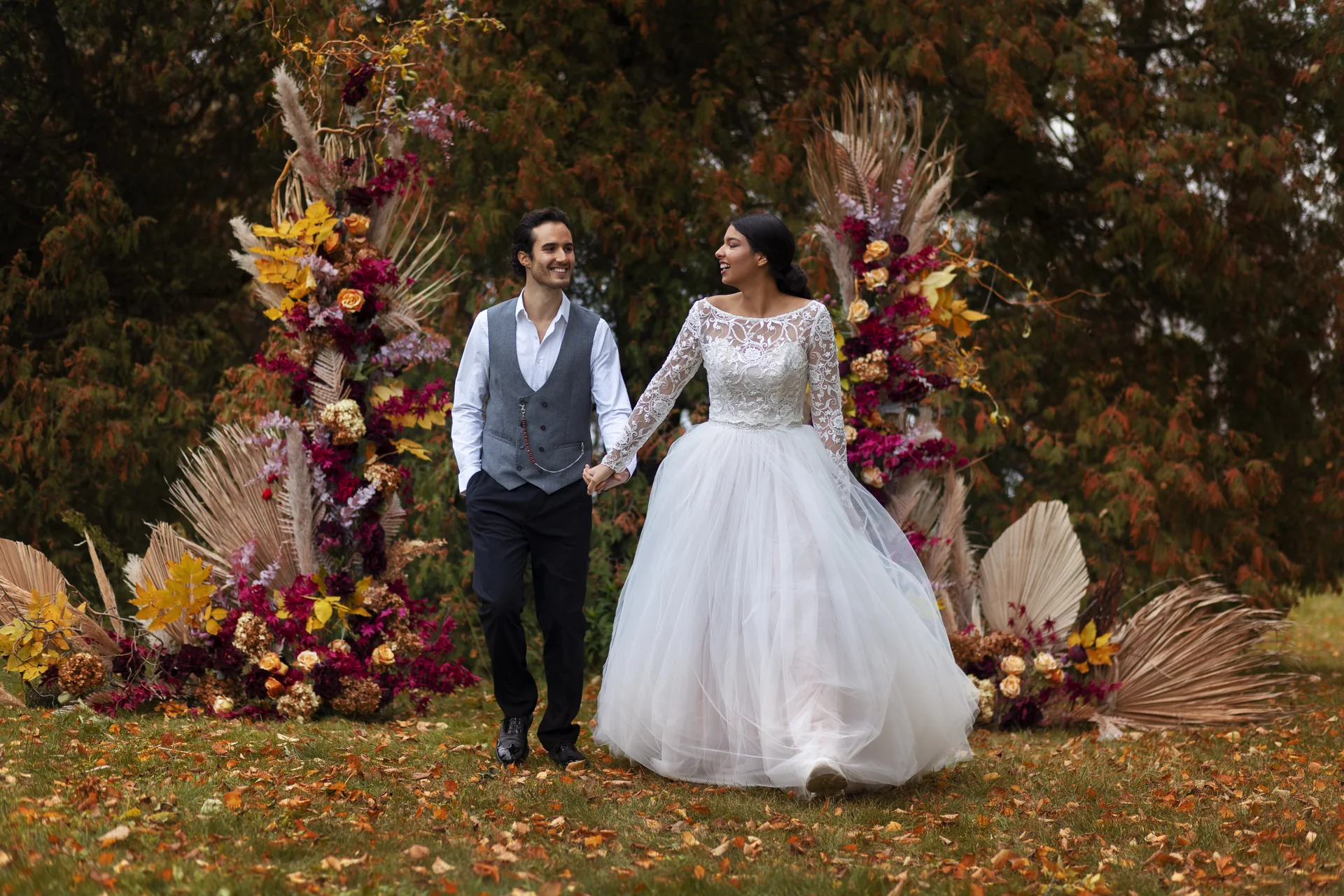 Wedding couple holding hands beside floral arrangements